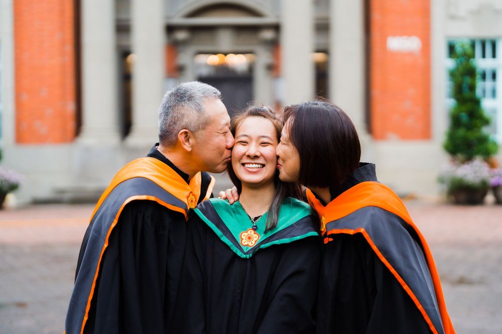 Family members in academic regalia share an emotional graduation moment outside a campus building.