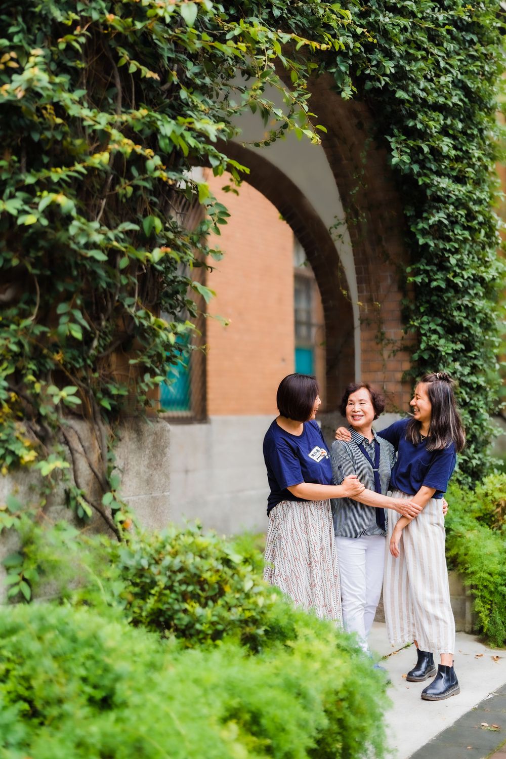 Three people share a joyful moment under an ivy-covered archway.