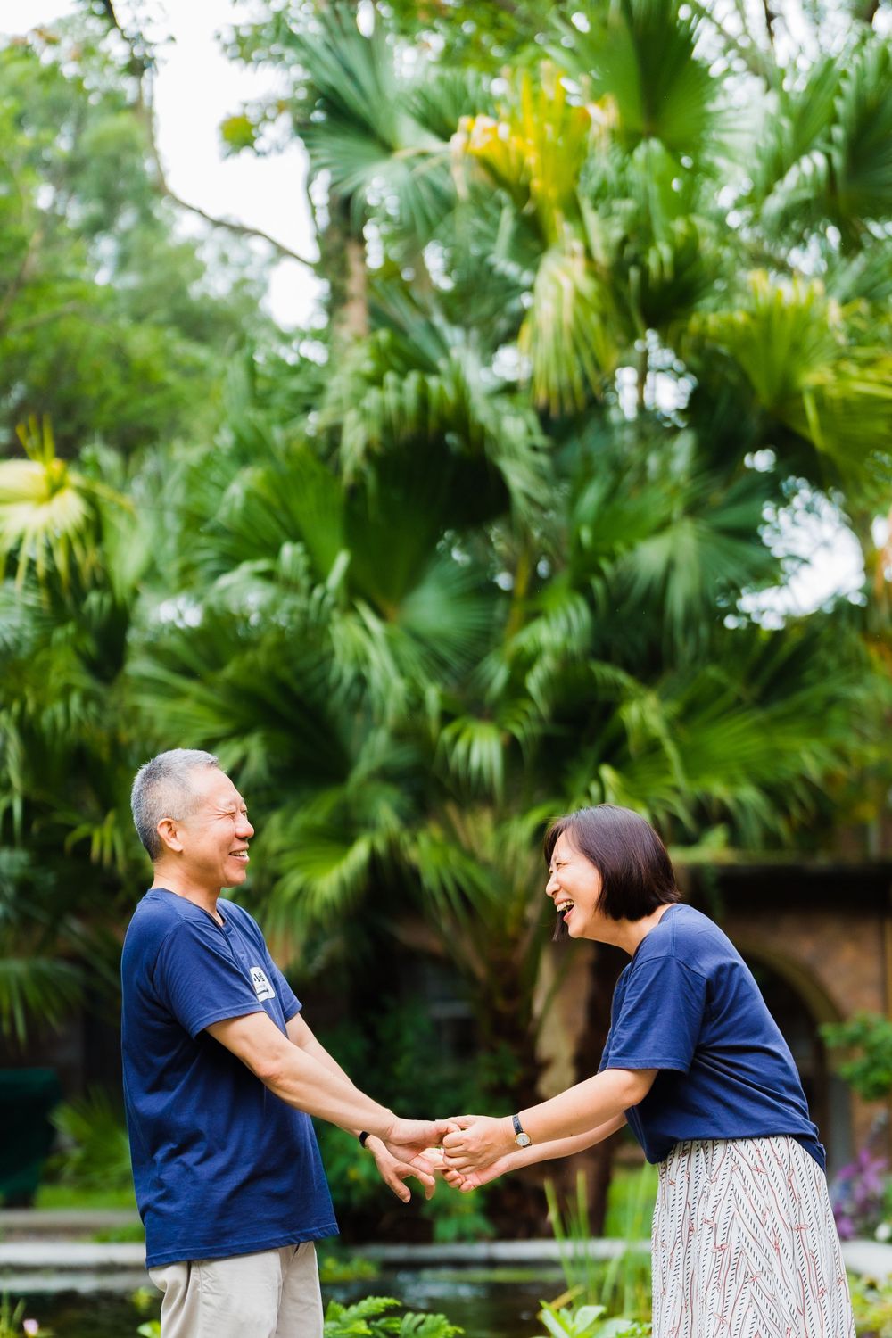 Two people share a joyful moment holding hands in a tropical garden setting.