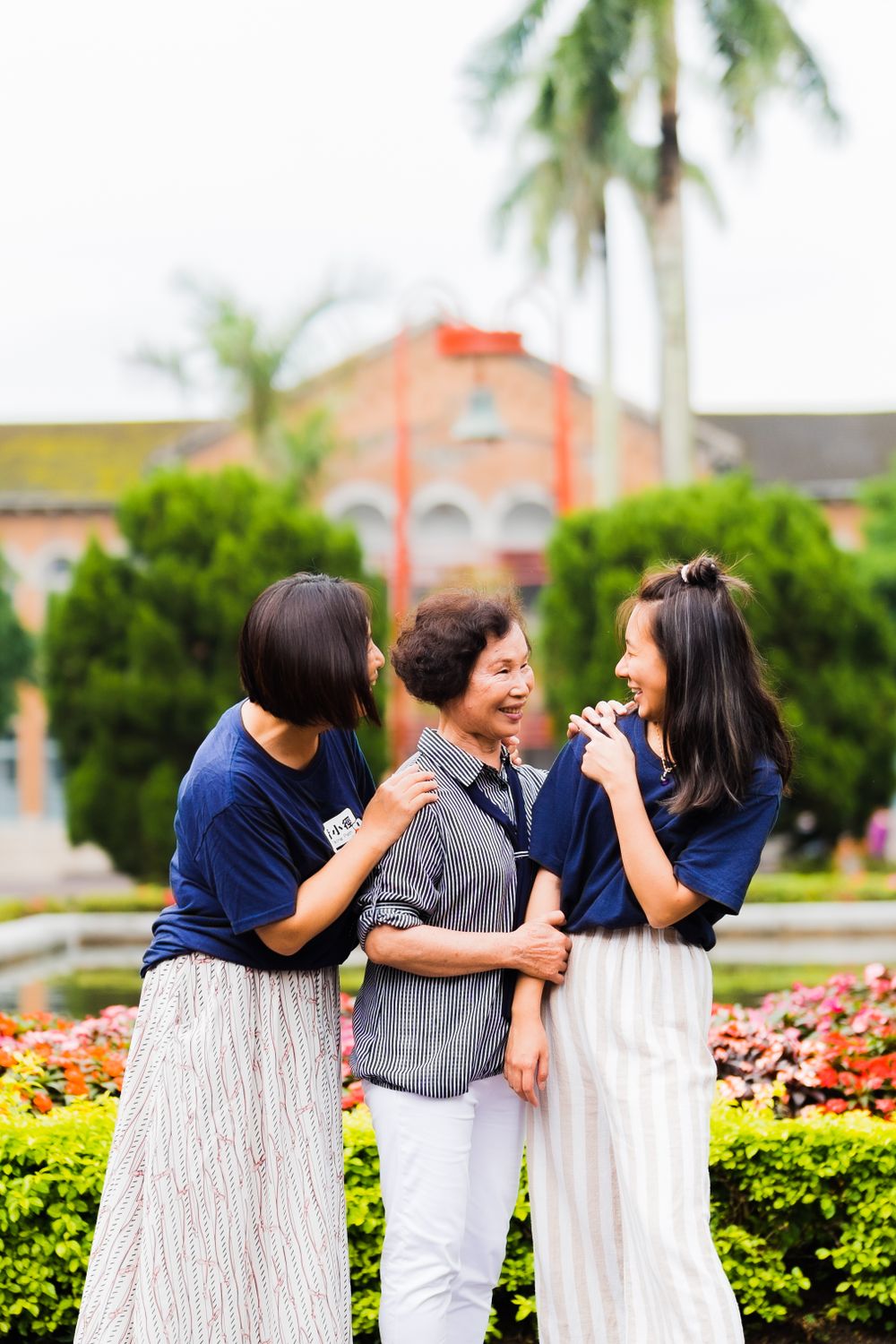 Three friends share a candid moment of laughter in front of a scenic campus garden.