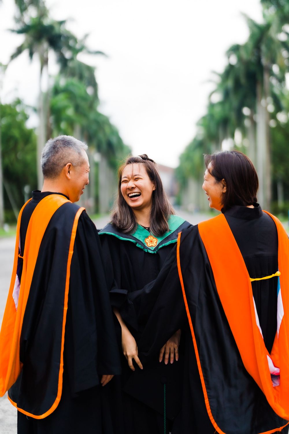 Candid moment of laughter between graduate and professors wearing academic regalia outdoors.