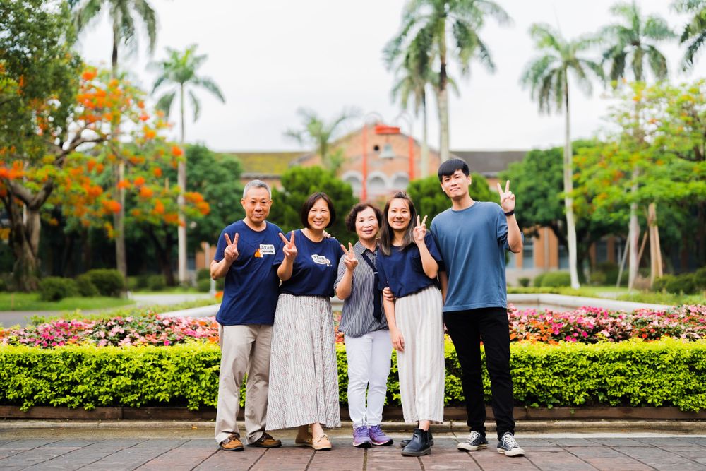 Group photo of friends in coordinated outfits standing in front of a tropical university landscape.