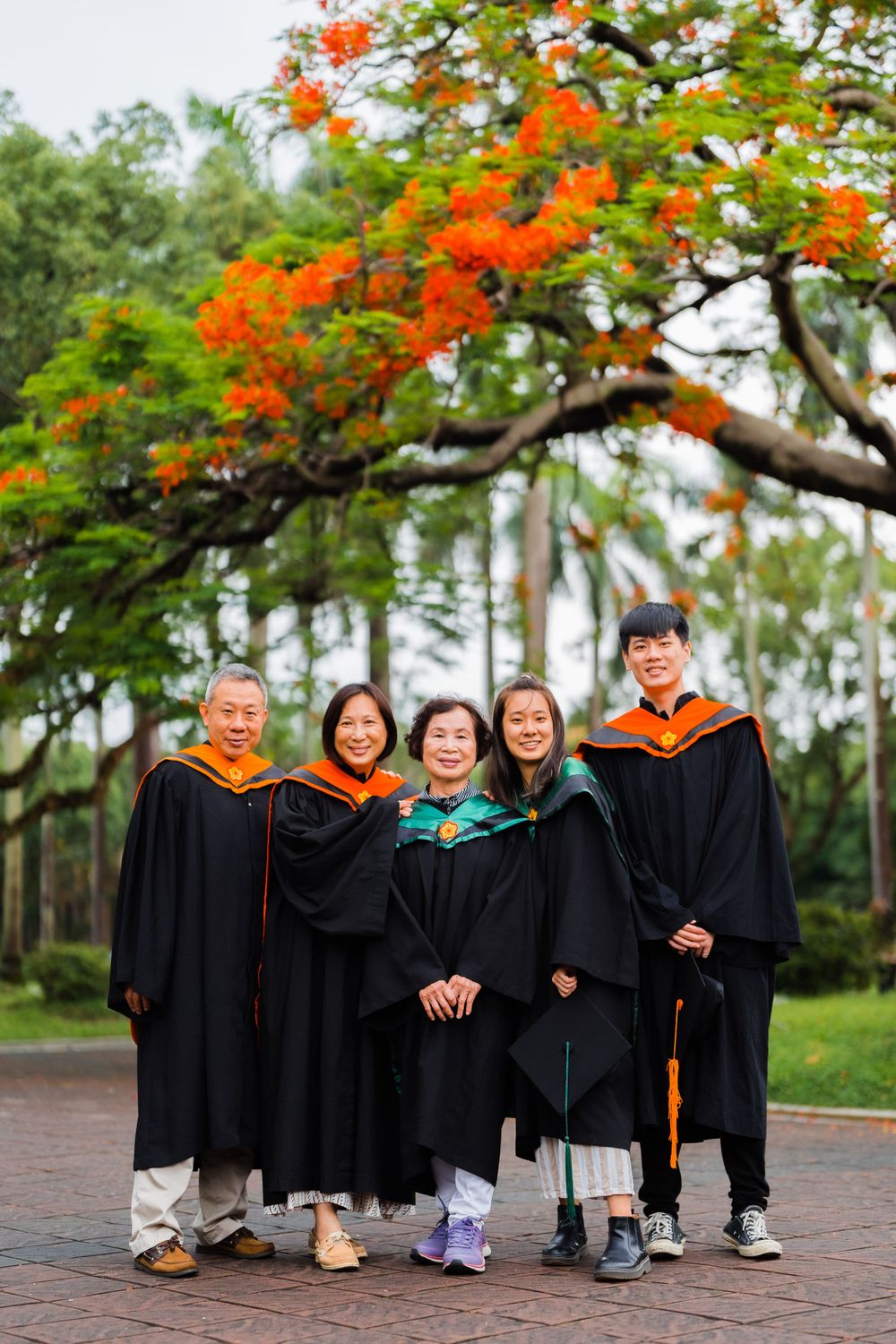 Group of graduates in academic regalia pose together under blooming orange trees.