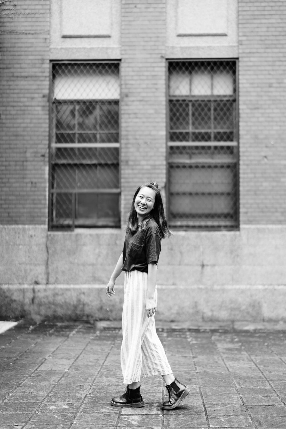 A joyful dance pose in black and white against a brick wall with barred windows.