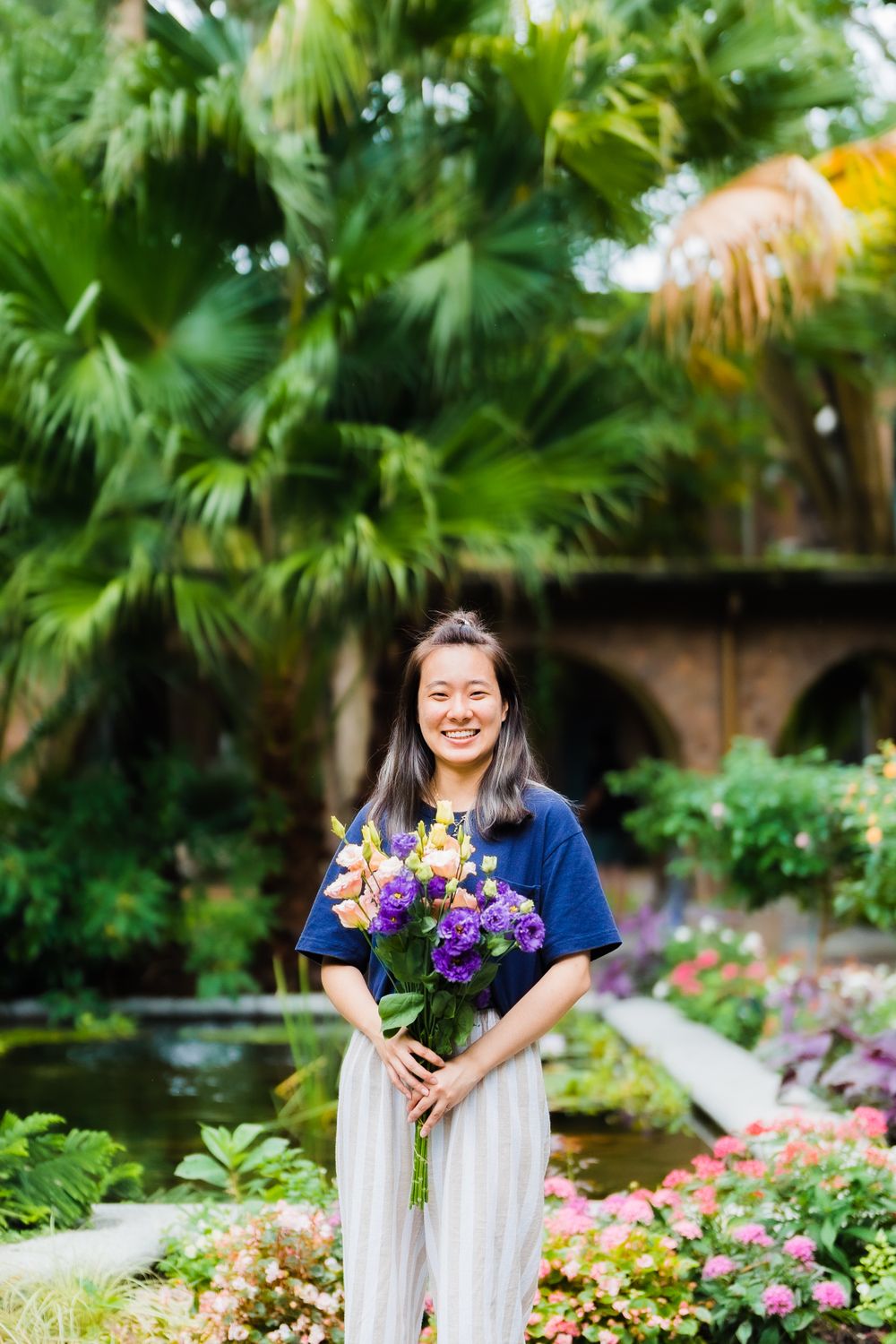 A person holding a colorful bouquet of flowers stands in a lush garden courtyard.
