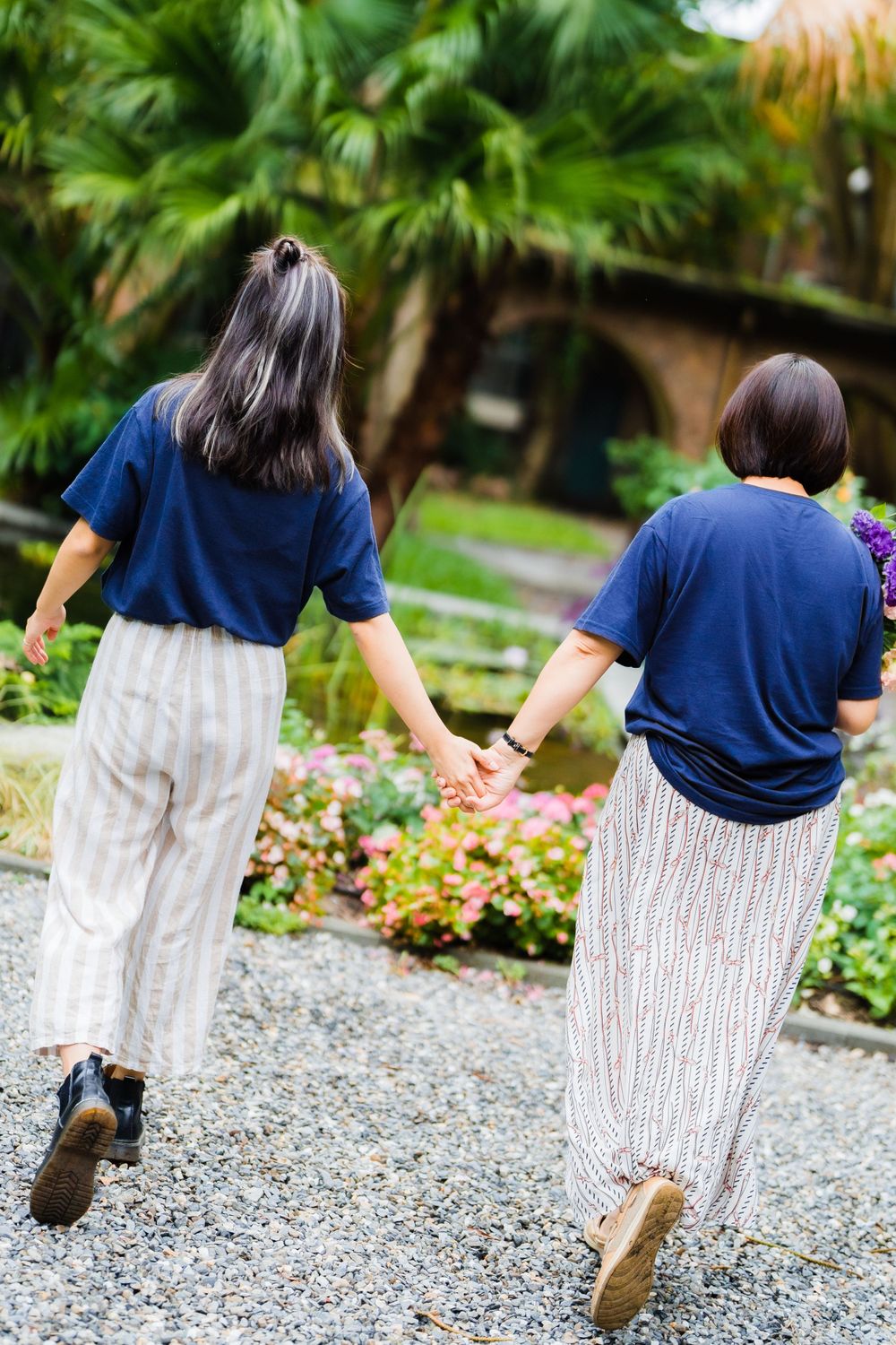 Two people in matching blue shirts walk hand in hand down a gravel garden path.