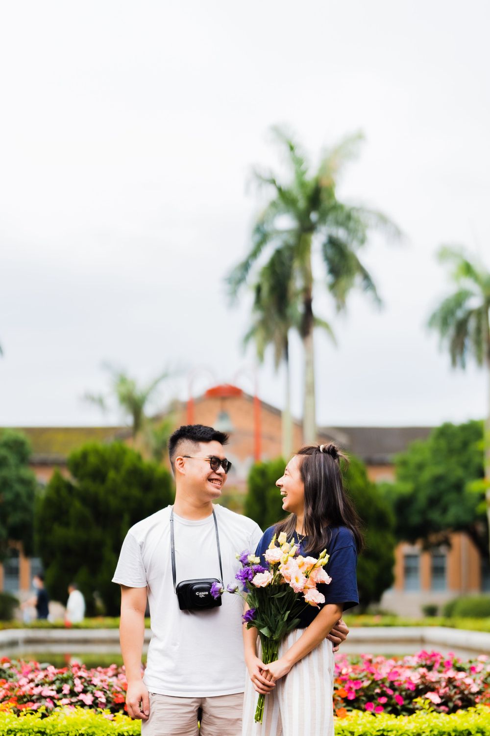 Candid moment between two people holding flowers in a tropical garden setting.
