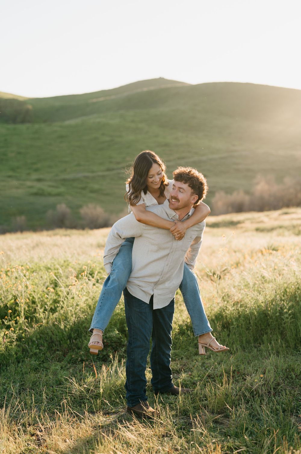 A couple playfully spins and embraces in a sunlit meadow during golden hour, creating a romantic outdoor moment.