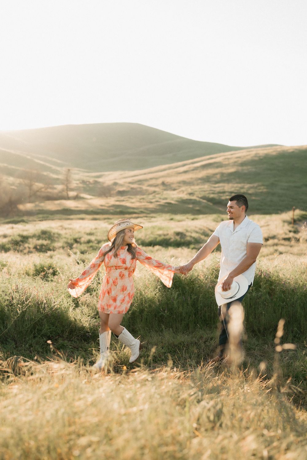 A couple runs playfully through a golden meadow at sunset holding a flowing fabric that catches the breeze.