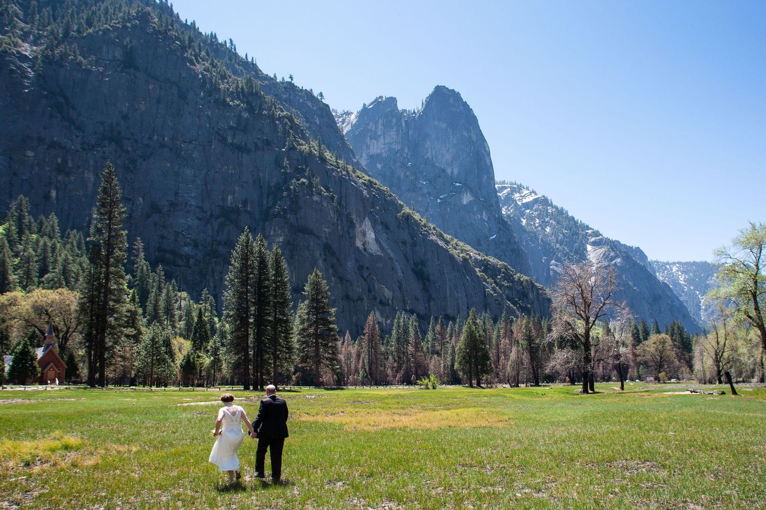 Wedding couple stands in meadow with dramatic mountain peaks of Yosemite in background.