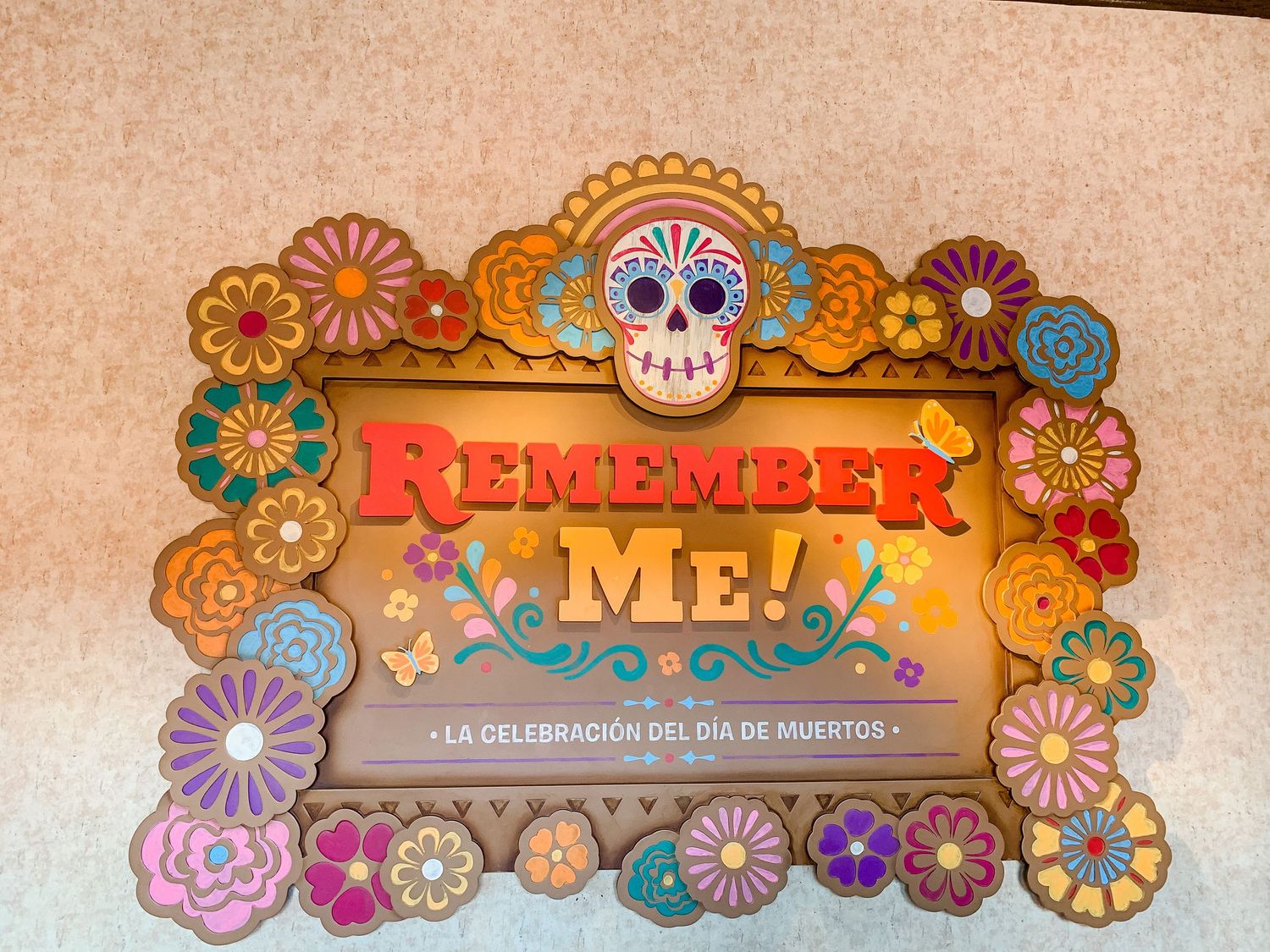 Colorful Coco-themed 'Remember Me' sign decorated with sugar skulls and vibrant flowers.