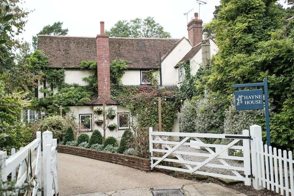 Charming English cottage with white gate entrance and climbing vines on brick exterior.