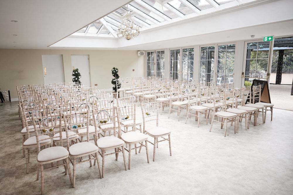 Light-filled wedding ceremony venue with rows of elegant white chairs under a glass ceiling skylight.