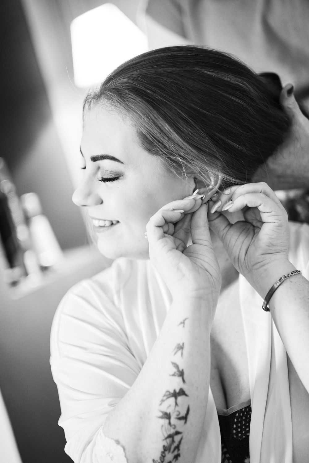 Black and white photo of someone putting on earrings during wedding preparations.