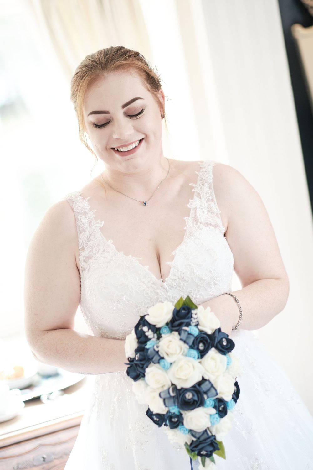 Radiant bride in lace wedding dress holds blue and white floral bouquet.