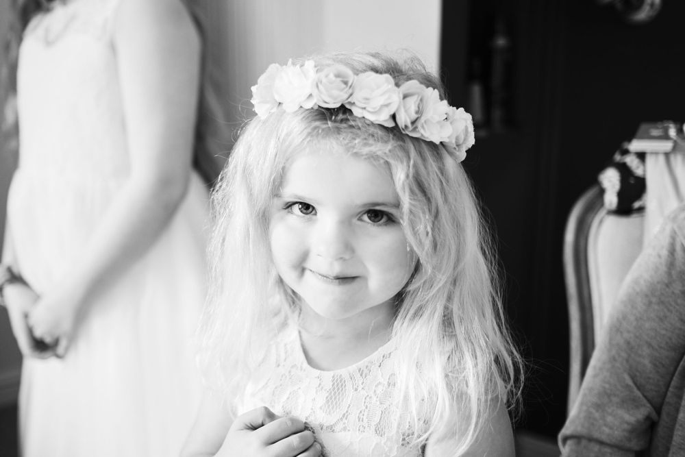 Black and white portrait of flower girl wearing floral crown at wedding.
