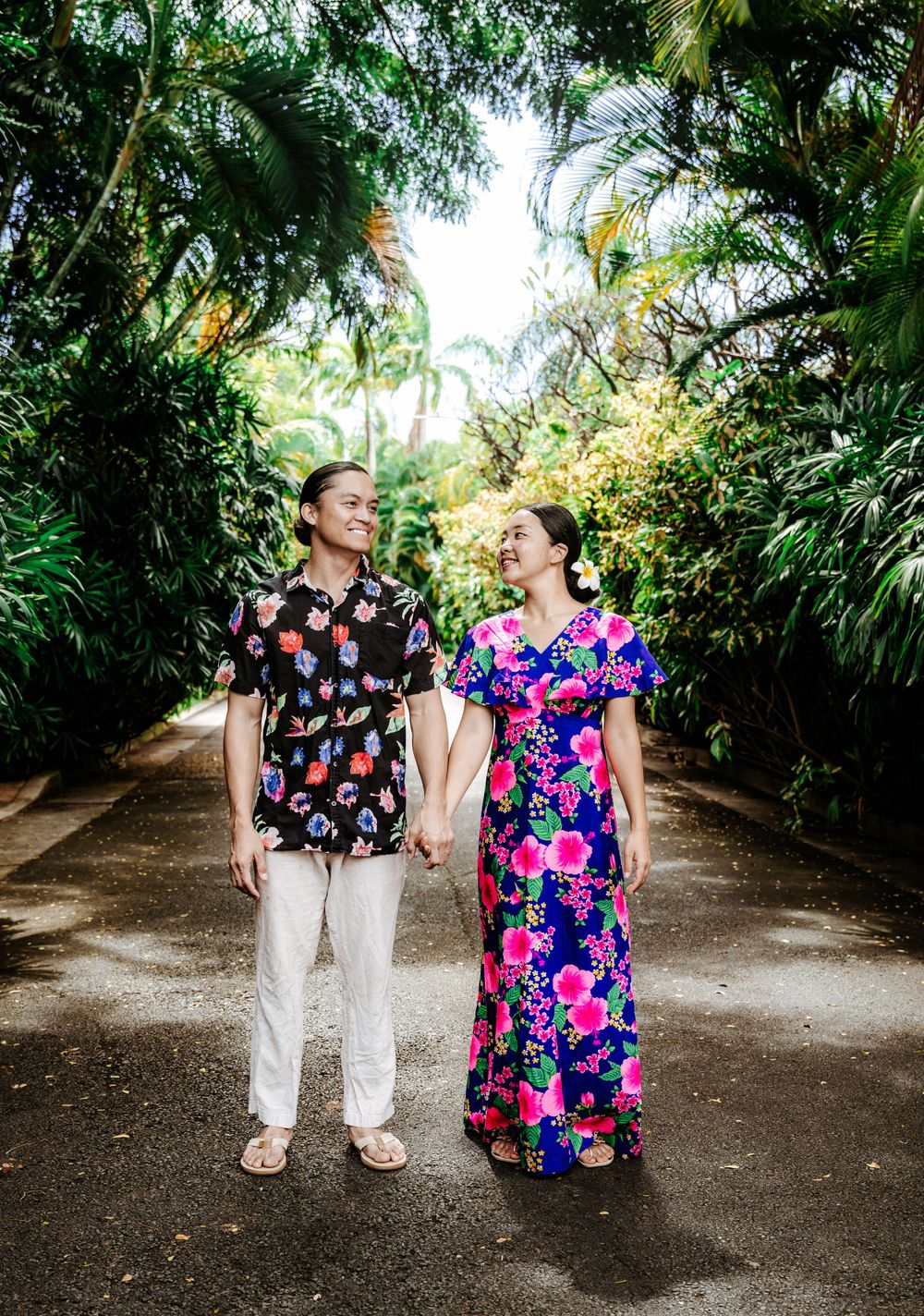 A couple in floral prints walking together on a tropical palm-lined pathway.