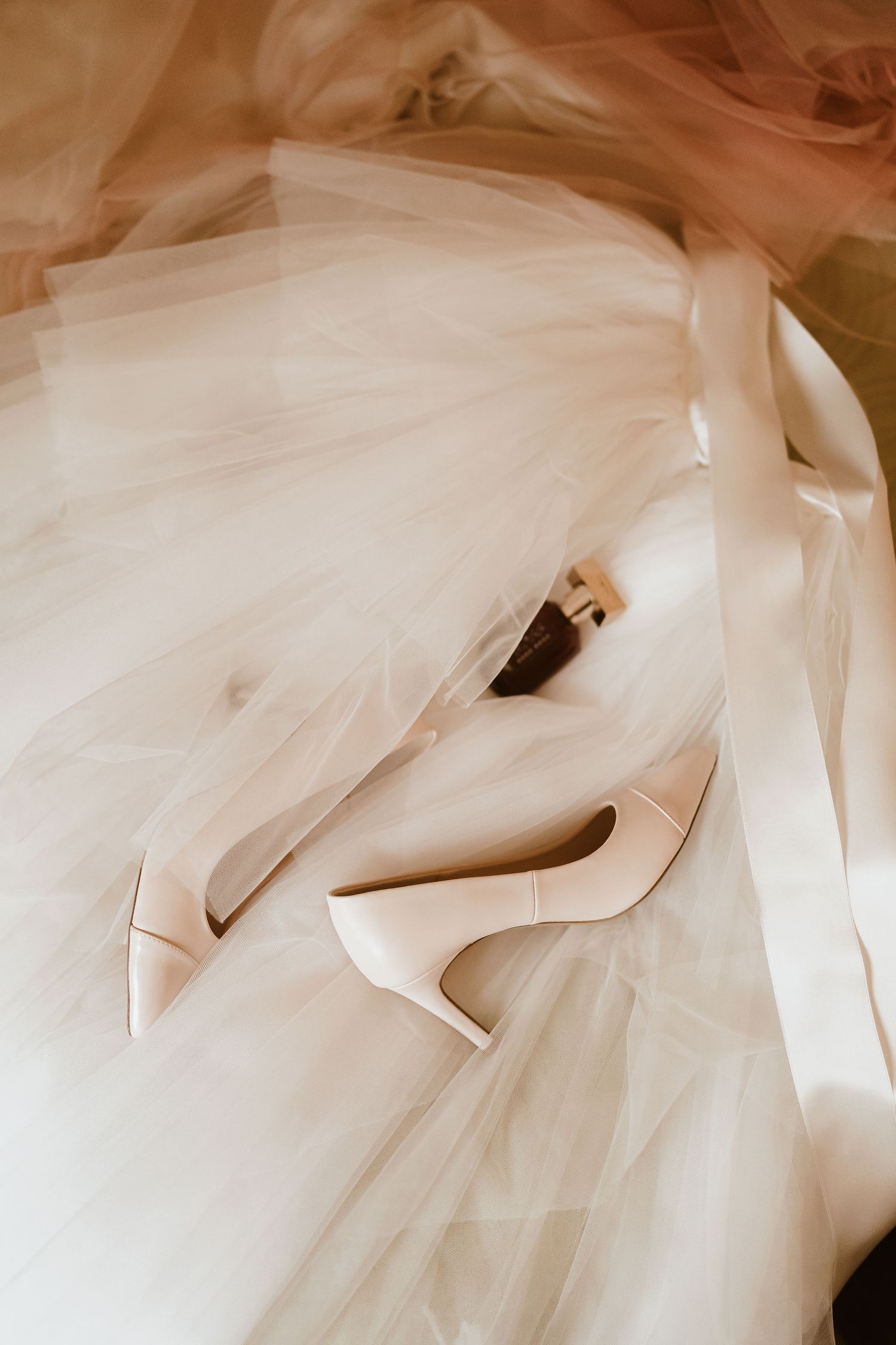 Elegant white bridal heels rest delicately on flowing tulle fabric.