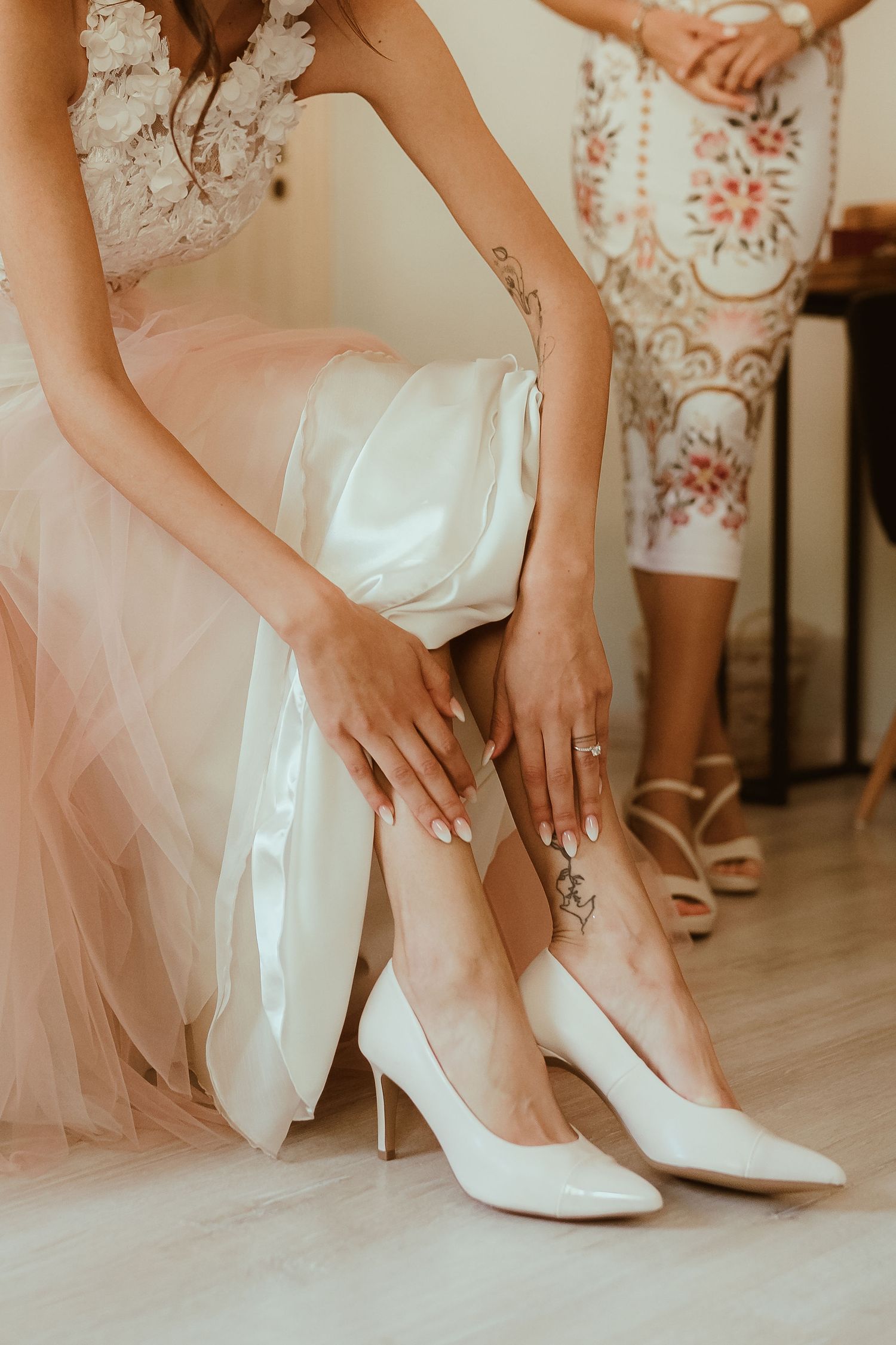 Detail shot of a bride putting on white heels while wearing a lace and tulle wedding dress.