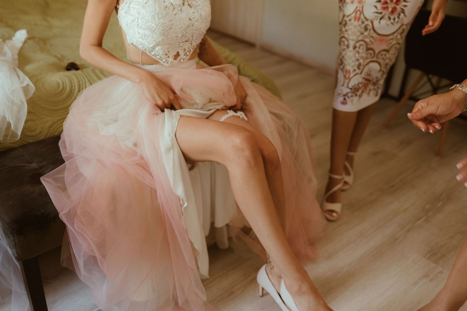 Candid moment of wedding dress preparation showing tulle skirt and white heels on wooden floor.