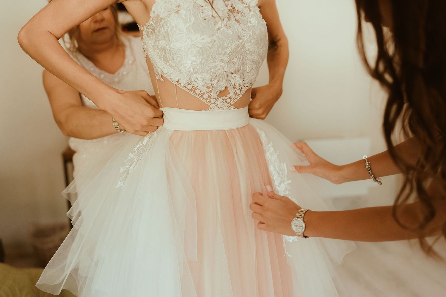 Close-up detail of hands adjusting a pink and white tulle wedding dress waistline.
