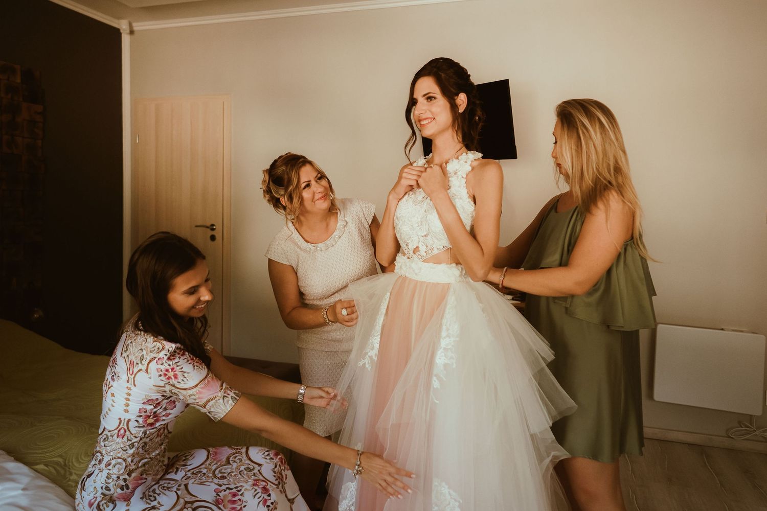 Wedding preparation scene showing final dress adjustments in a cozy indoor setting.