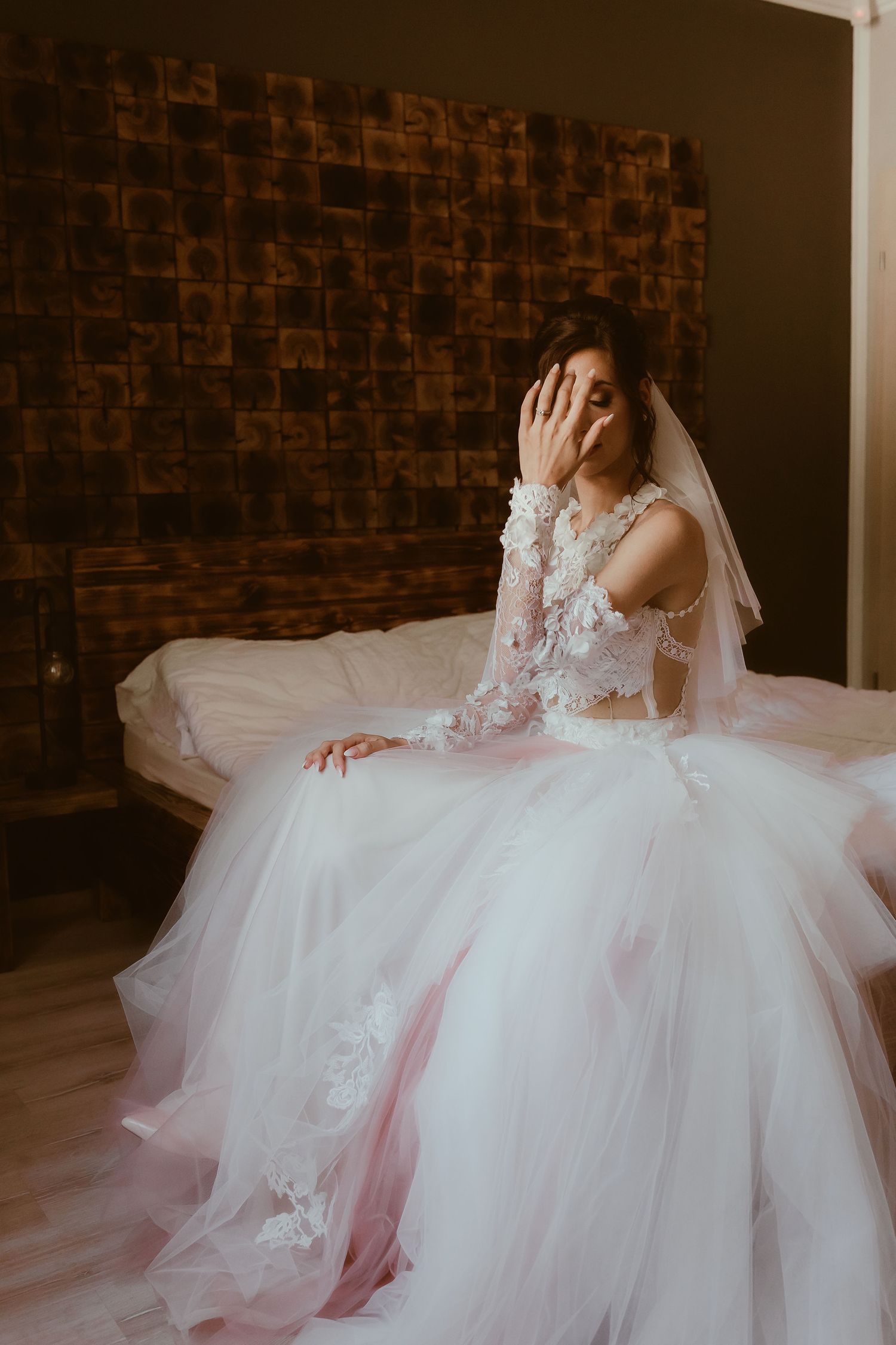 Artistic bridal portrait against textured brown wall showing flowing tulle wedding dress.