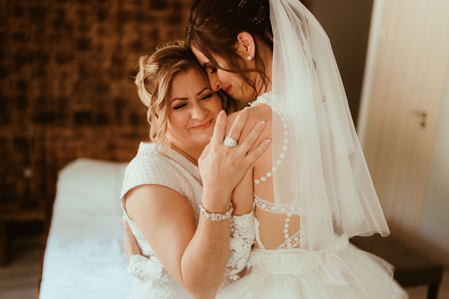 Two women share an intimate emotional moment in white dresses during a wedding celebration.