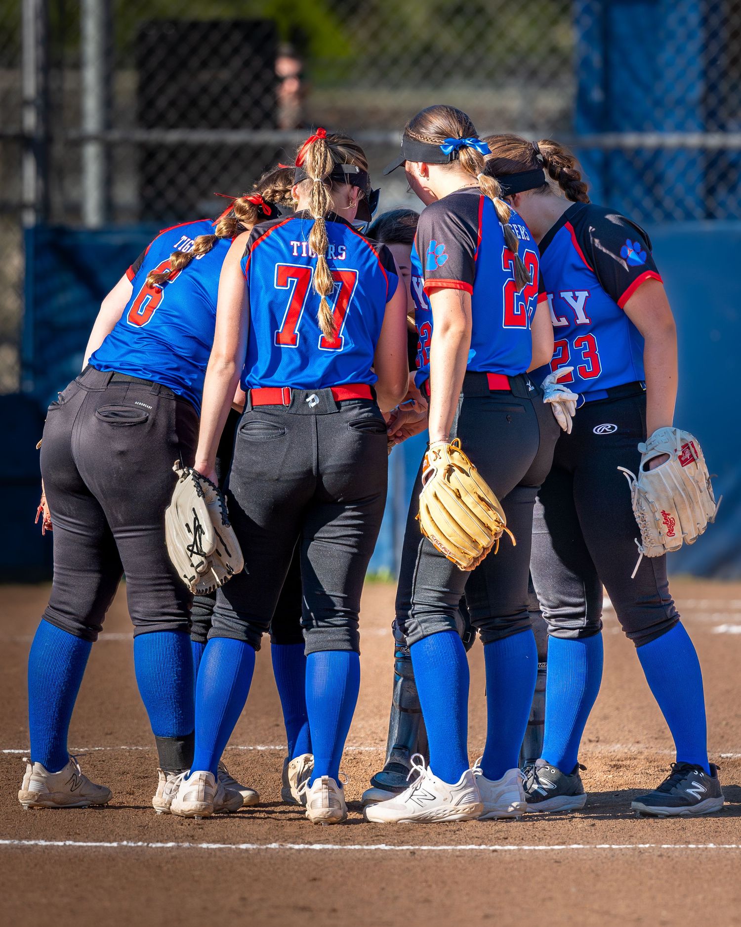 Softball team huddled together on field wearing blue and red uniforms.