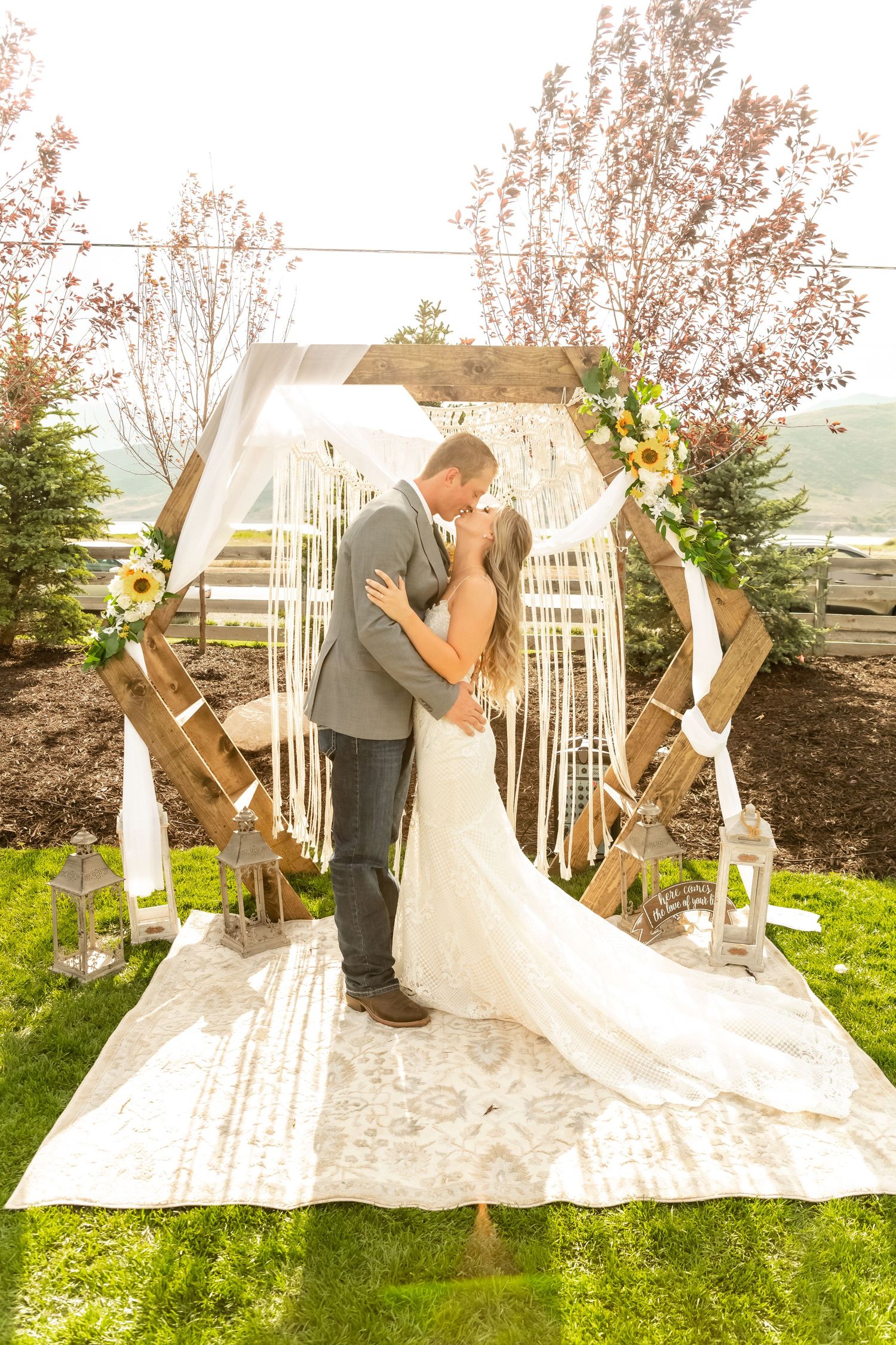 Romantic outdoor wedding ceremony under a white arch decorated with flowers and greenery.