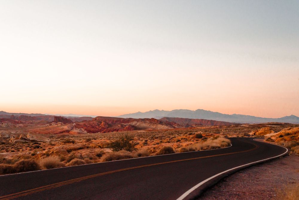 A winding desert road stretches toward mountains under a pastel sunset sky.