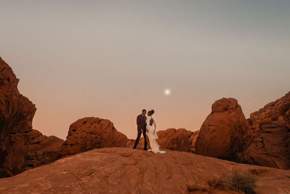 Wedding couple poses on red rock formations during sunset.