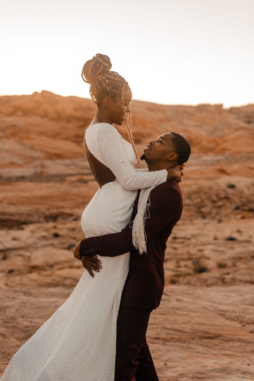 Wedding couple embraces in intimate moment against desert landscape at sunset.
