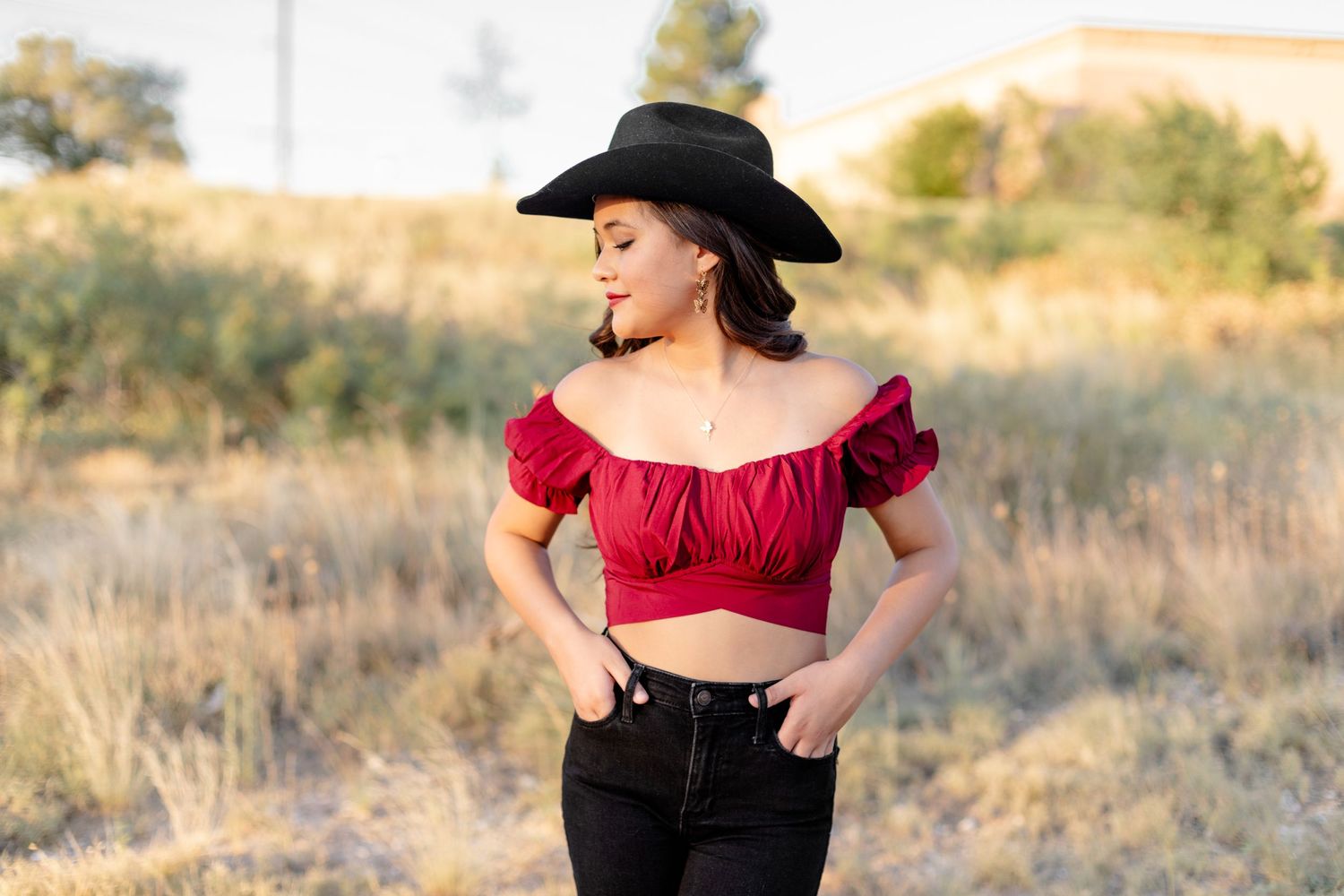 Woman in red crop top and black hat poses in desert landscape setting.