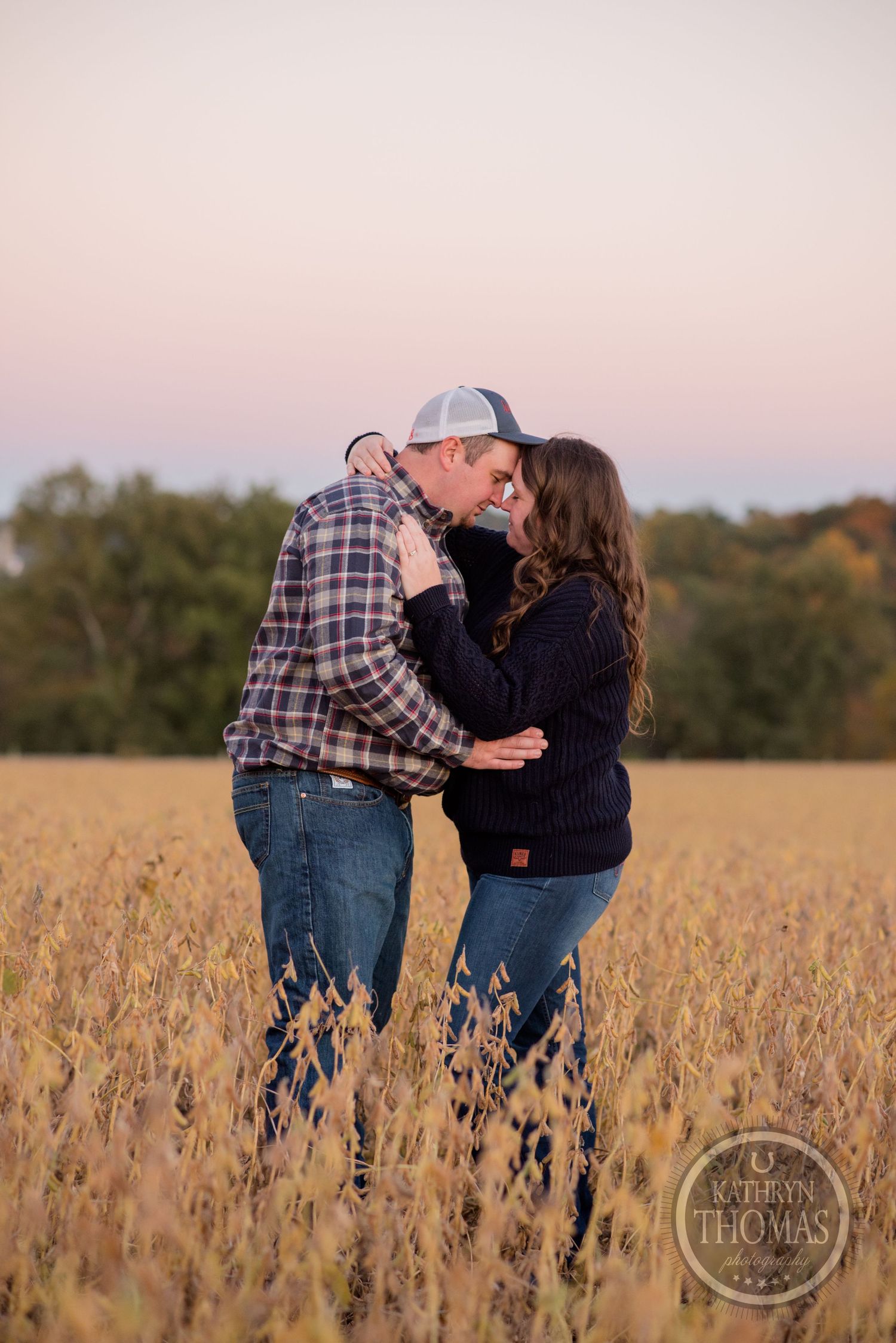 Affectionate couple embracing in tall grass field during sunset.