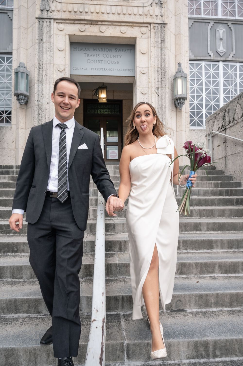 Newlyweds descending courthouse steps while holding hands and smiling.