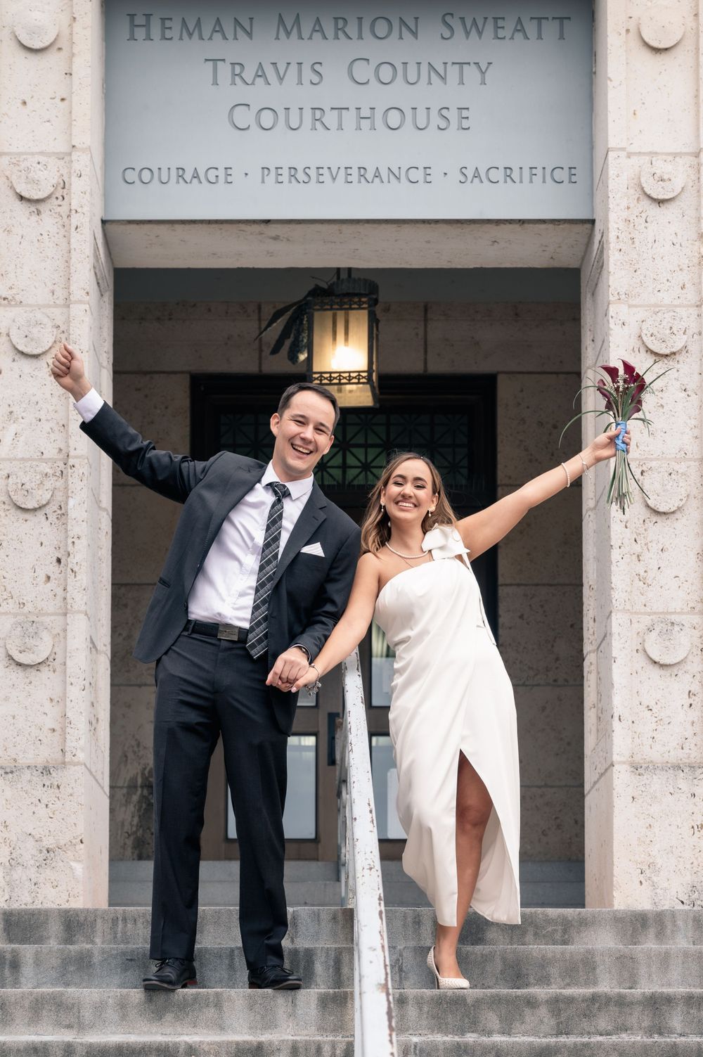 Celebratory couple with arms raised at Travis County Courthouse entrance.