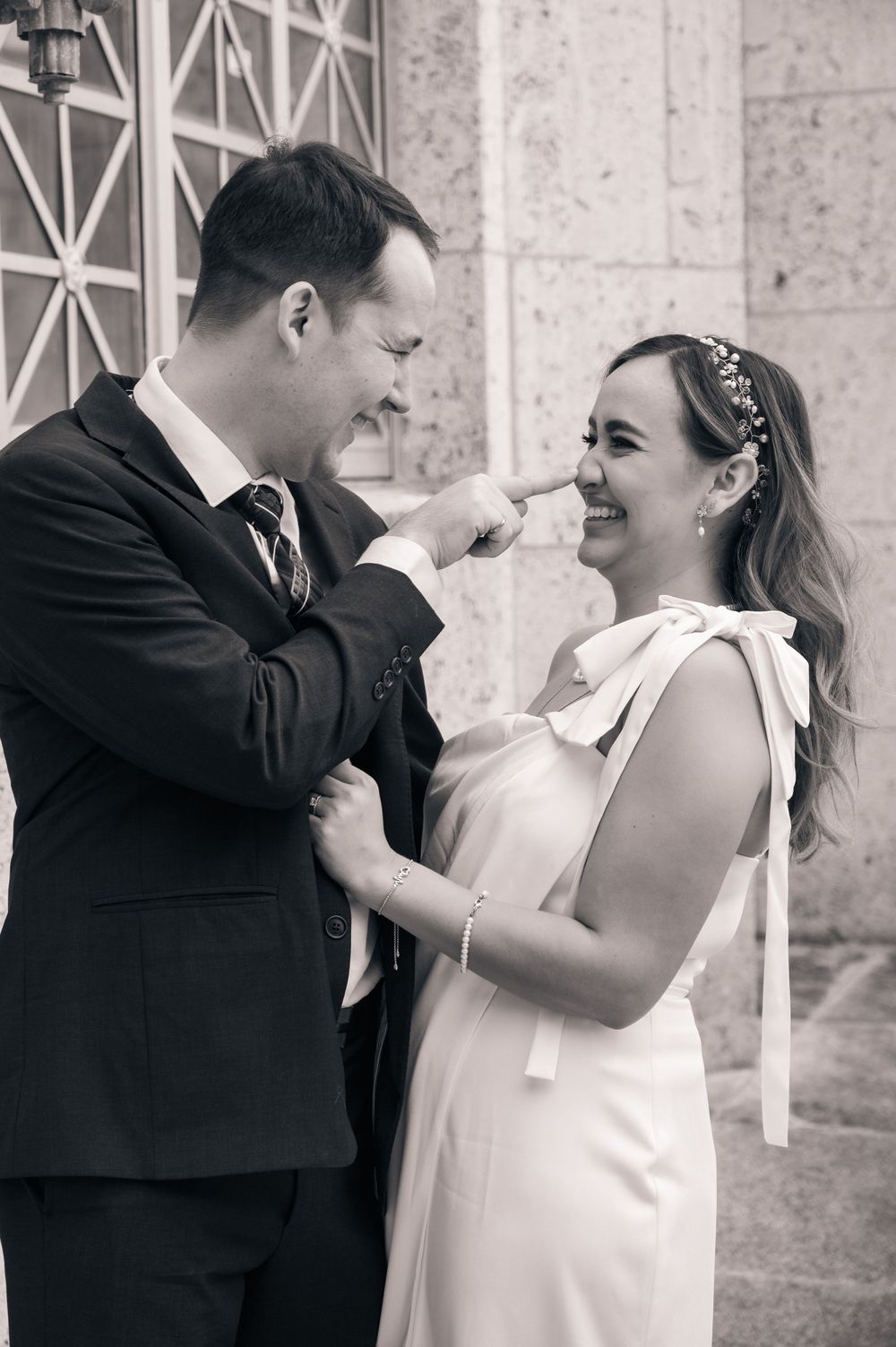 Black and white portrait of couple sharing a playful moment against stone wall.