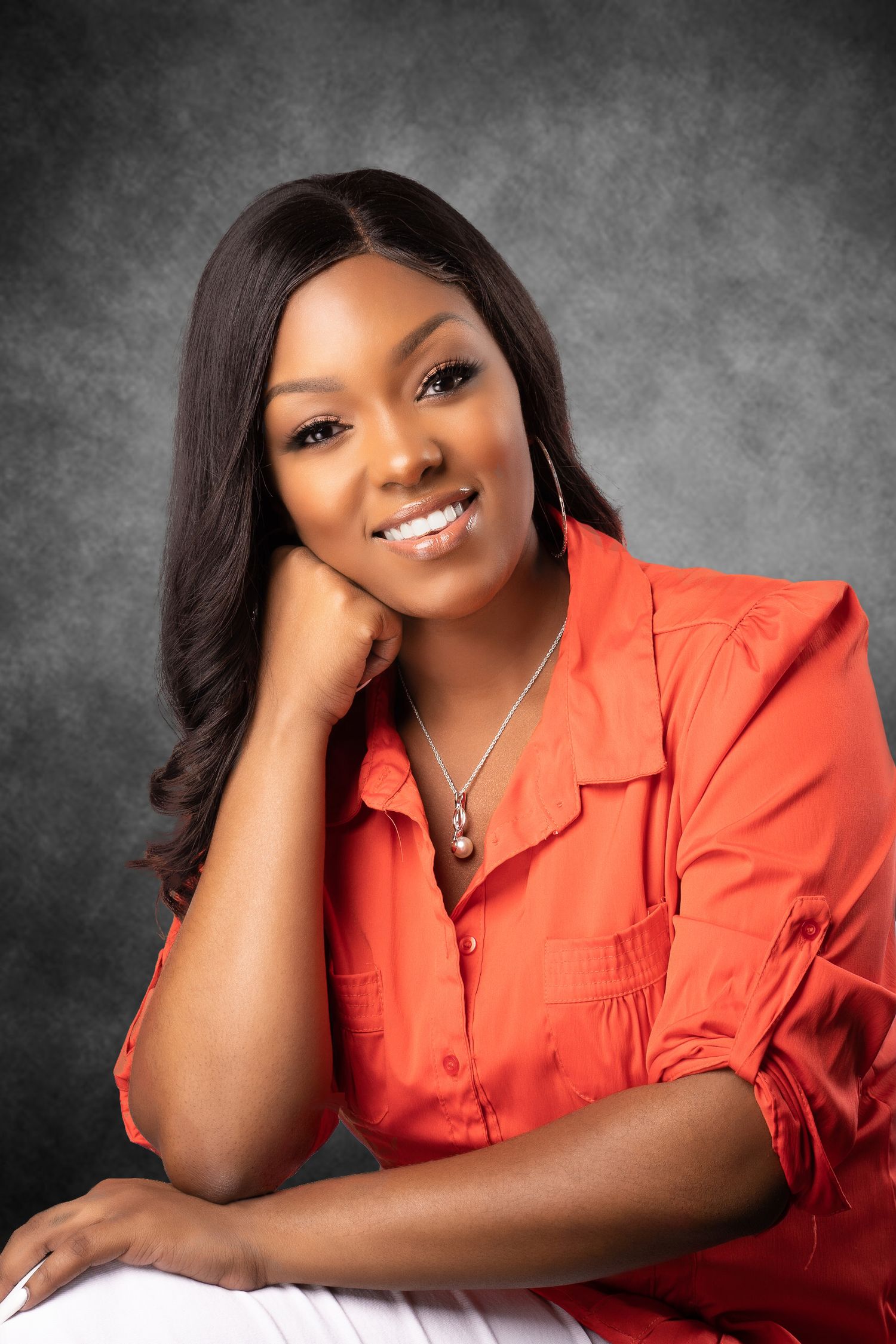 Studio portrait of a person in coral blouse with elegant pose against grey background.