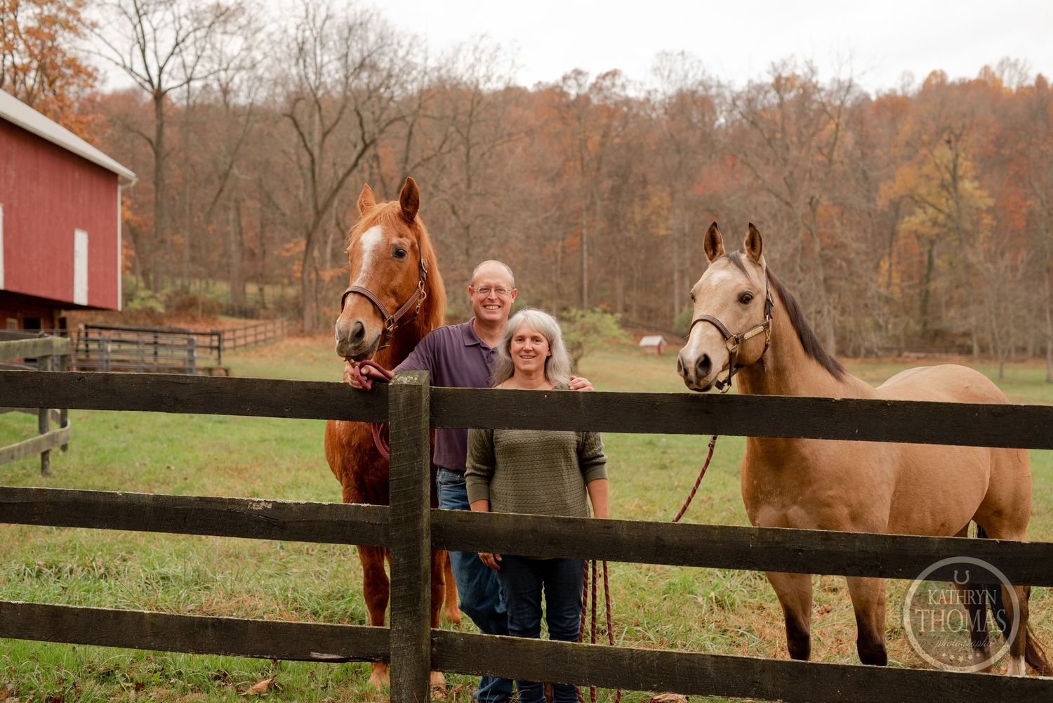 Two horses lean over a wooden fence to greet visitors at a farm.