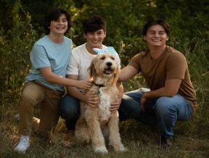 Family group sits casually on grass with their fluffy white dog in outdoor setting.