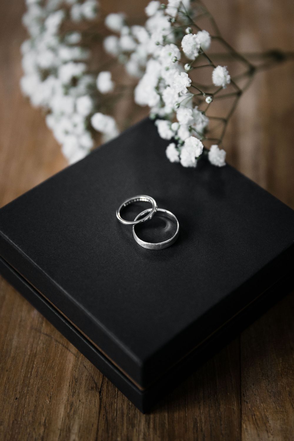 Silver wedding bands displayed on black box with baby's breath flowers as decoration.
