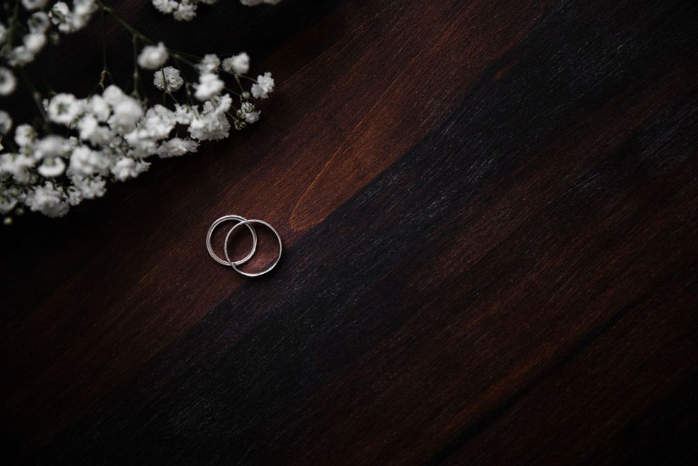 Two silver wedding rings placed on a dark wooden surface with baby's breath flowers in the background.