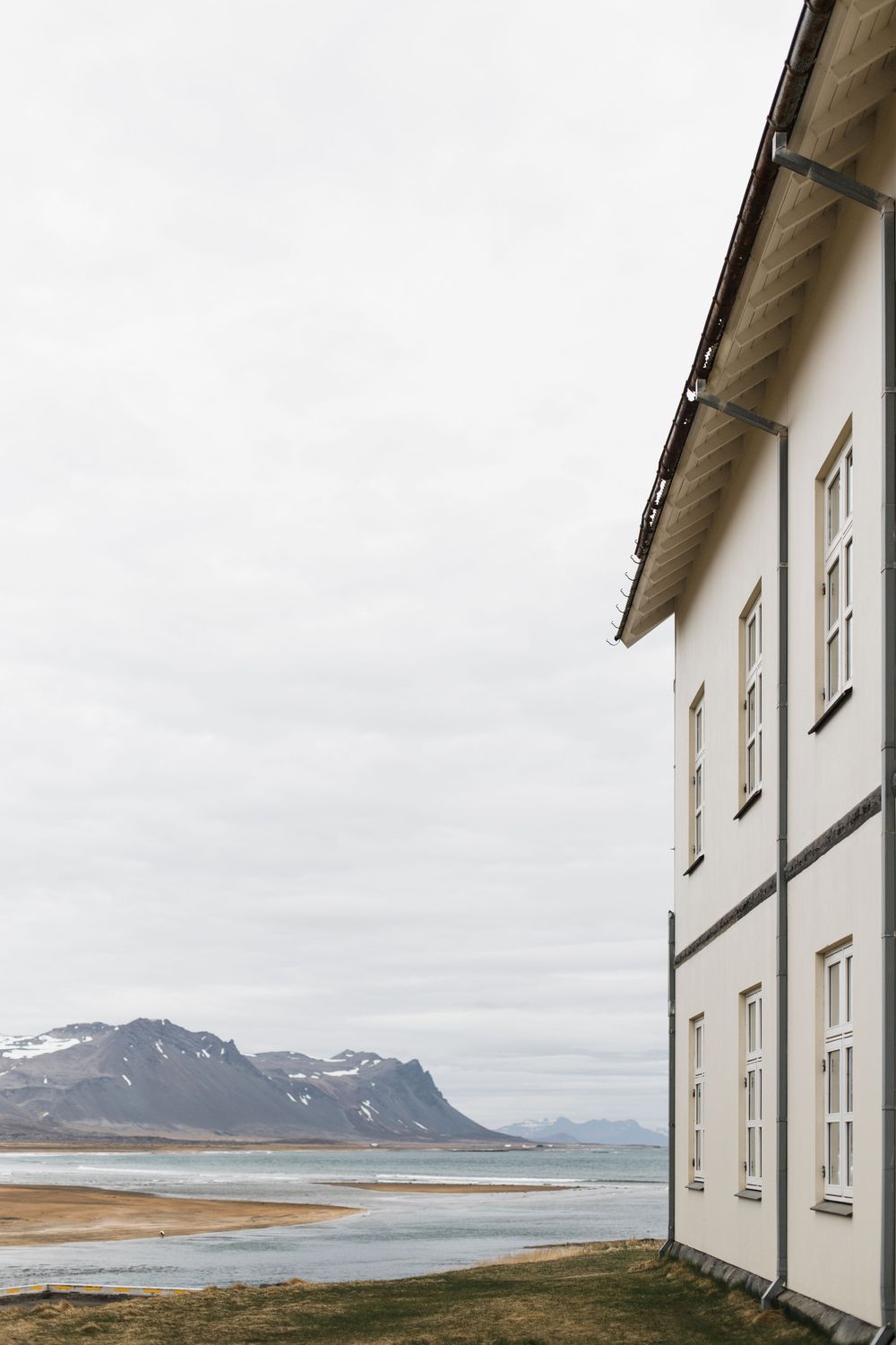 White building with windows overlooks a mountainous coastline in Iceland under an overcast sky.