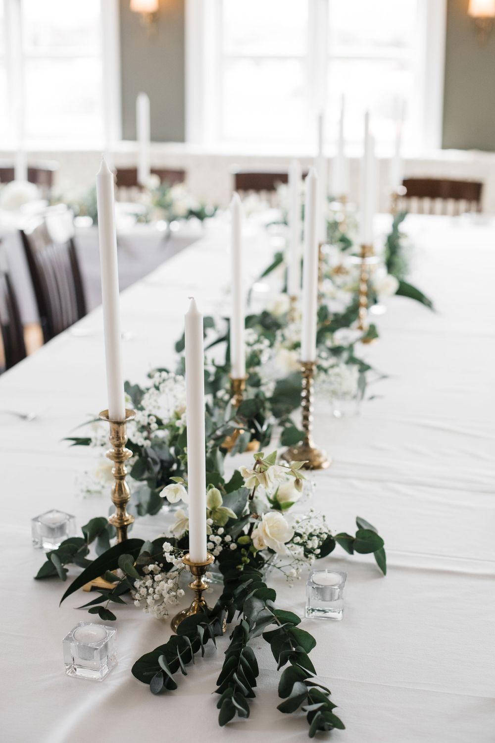 White taper candles and floral arrangements create an elegant table centerpiece with greenery.
