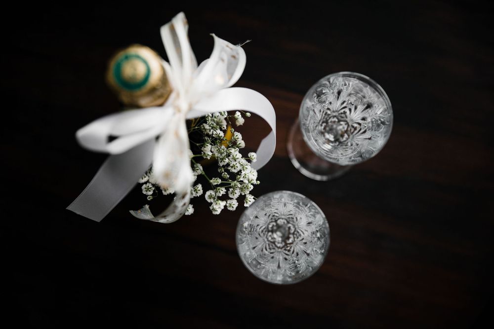 Wedding details with champagne glasses and white ribbon on dark wood surface.