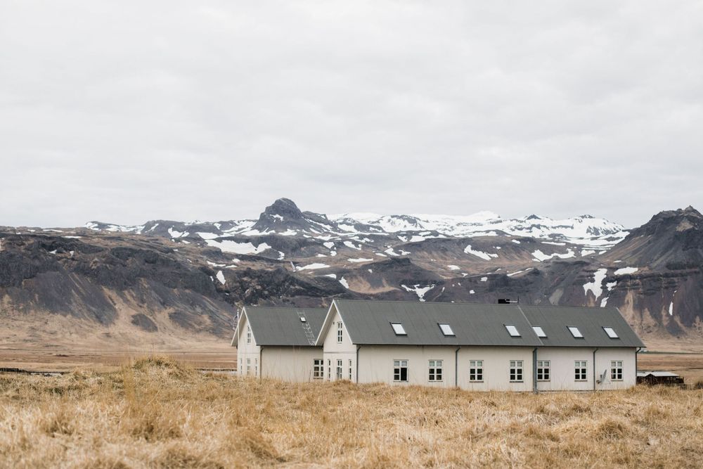 Long white church building nestled beneath snow-capped mountains in a rural Icelandic landscape.