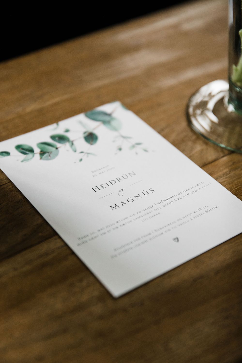 A minimalist wedding invitation with green watercolor eucalyptus design on a wooden table.