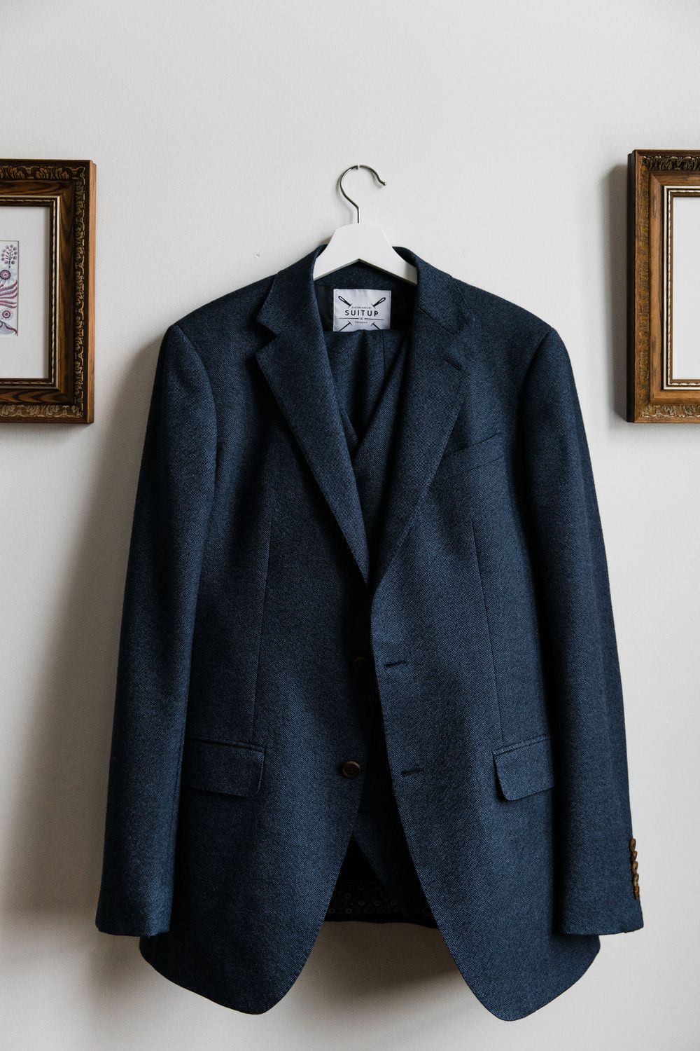 Navy blue suit jacket hanging on display between framed artwork.