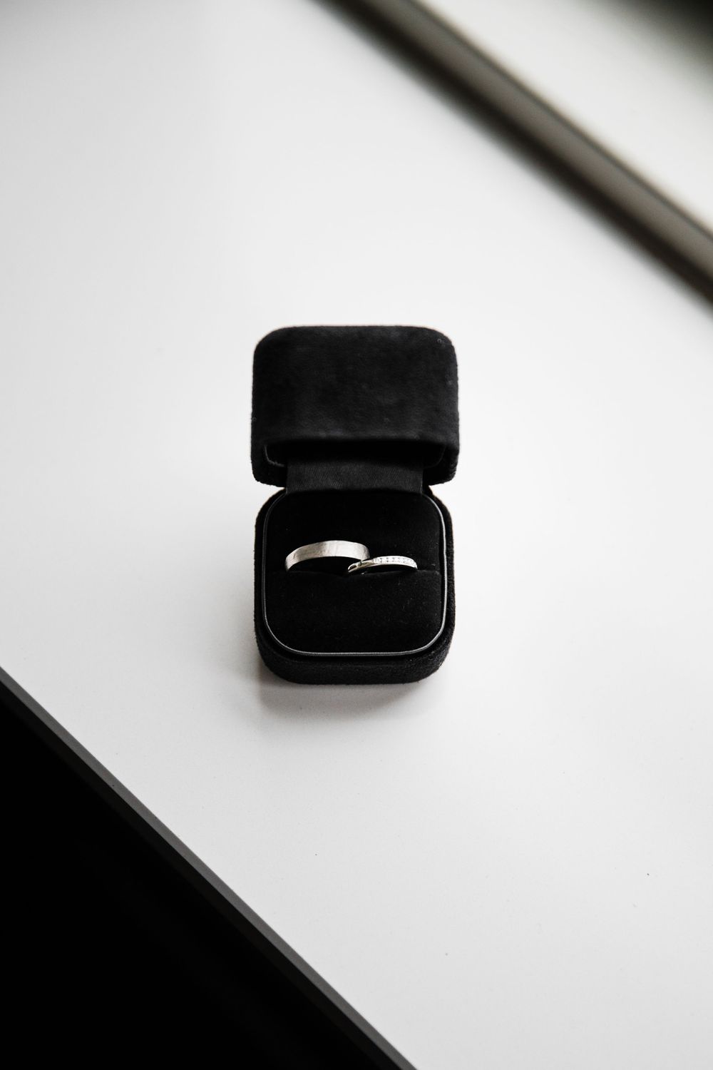 A silver wedding ring sits in an elegant black velvet ring box against a white background.